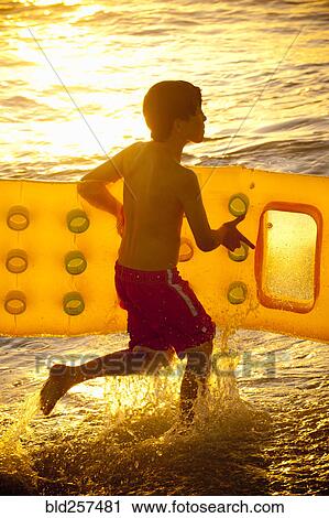 Caucasian boy running into ocean carrying inflatable raft View Large Photo Image Stock Image - Caucasian boy running into ocean carrying inflatable raft. Fotosearch