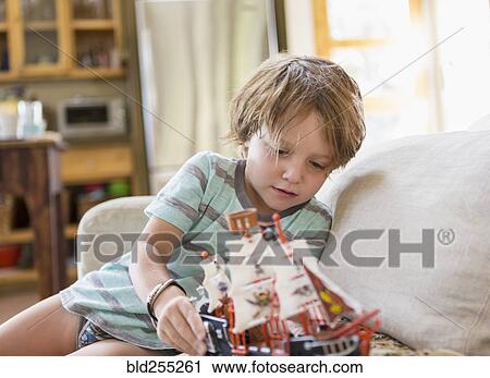 Stock Image - Caucasian boy sitting on sofa playing with toy boat. Fotosearch