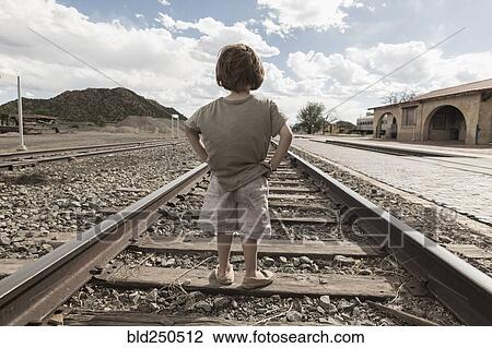 Stock Image - Caucasian boy standing with hands on hips on train track. Fotosearch