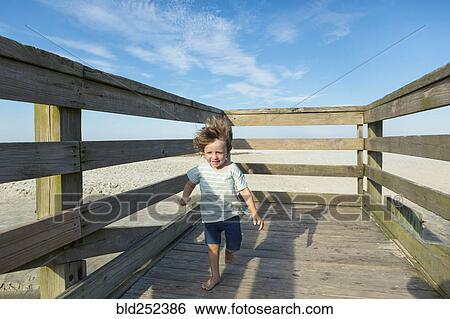 Stock Photograph - Caucasian boy walking on windy boardwalk. Fotosearch