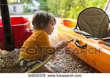 Stock Photo - Caucasian boy washing kayak with hose. Fotosearch