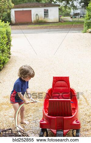 Stock Photography - Caucasian boy washing red wagon with hose. Fotosearch