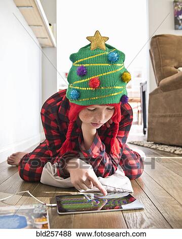 Stock Photo - Caucasian boy wearing Christmas tree stocking-cap using digital tablet on floor. Fotosearch