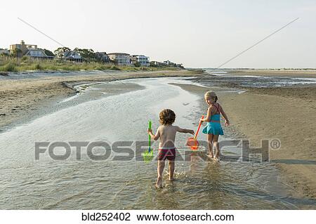 Stock Image - Caucasian brother and sister carrying nets on beach. Fotosearch