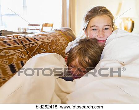 Stock Photography - Caucasian brother and sister cuddling in comforter. Fotosearch