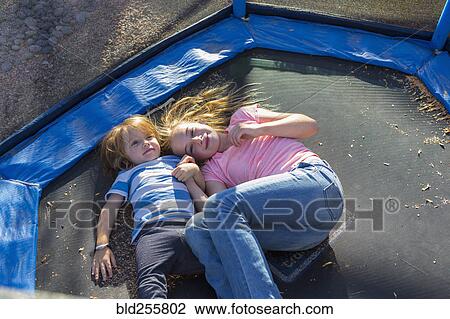 Stock Image - Caucasian brother and sister laying on trampoline. Fotosearch