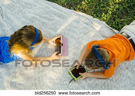 Stock Image - Caucasian brother and sister laying on blanket using technology. Fotosearch