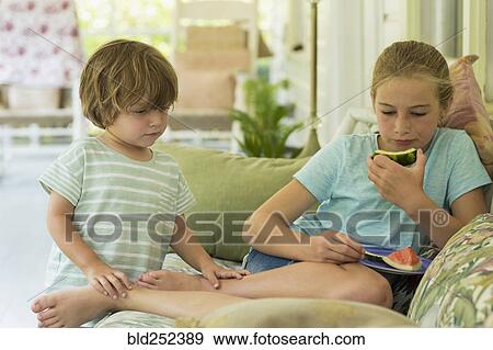 Stock Photo - Caucasian brother and sister watching digital tablet on sofa. Fotosearch