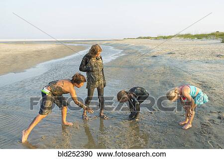 Stock Image - Caucasian brother and sisters covered in mud playing on beach. Fotosearch