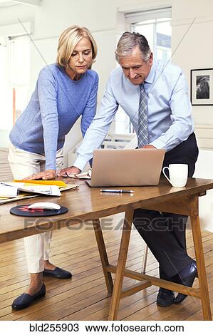 Stock Image - Caucasian business people leaning on table using laptop. Fotosearch