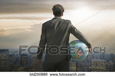 Stock Photo - Caucasian businessman holding globe overlooking cityscape. Fotosearch