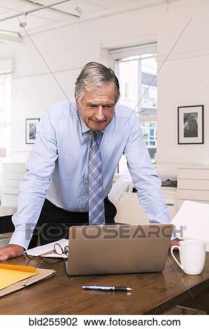 Stock Image - Caucasian businessman leaning on table using laptop. Fotosearch