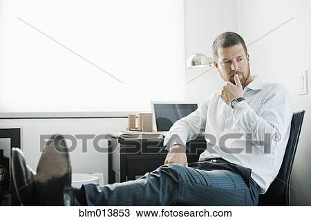 Stock Image - Caucasian businessman sitting at desk with feet up. Fotosearch