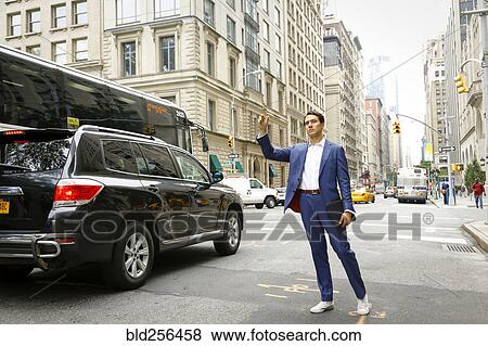 Stock Photo - Caucasian businessman standing in street hailing taxi. Fotosearch