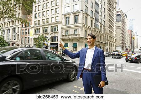 Stock Photo - Caucasian businessman standing in street hailing taxi. Fotosearch