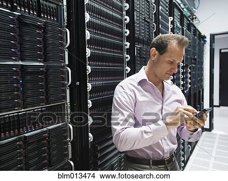 Picture - Caucasian businessman using cell phone in server room. Fotosearch