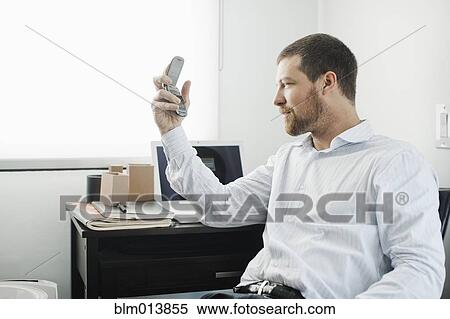 Stock Photography - Caucasian businessman using cell phone at desk. Fotosearch