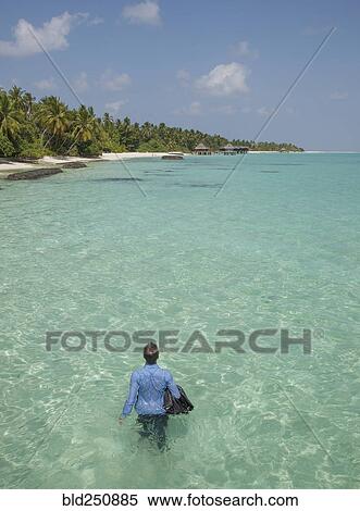 Stock Photography - Caucasian businessman walking in ocean. Fotosearch