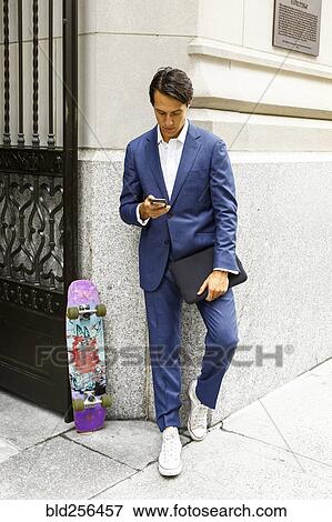 Stock Photo - Caucasian businessman with skateboard texting on cell phone. Fotosearch