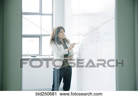 Stock Image - Caucasian businesswoman holding digital tablet and writing on whiteboard. Fotosearch