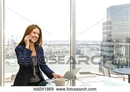 Stock Photo - Caucasian businesswoman talking on cell phone and using laptop. Fotosearch