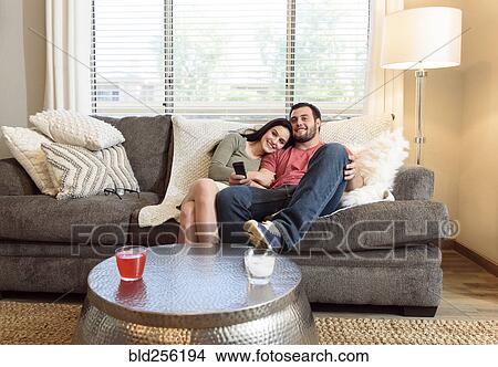 Picture - Caucasian couple cuddling on sofa watching television. Fotosearch