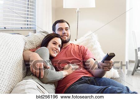 Stock Photograph - Caucasian couple cuddling on sofa watching television. Fotosearch