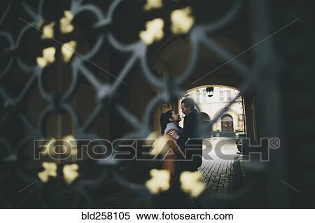 Stock Photography - Caucasian couple embracing in street behind gate. Fotosearch