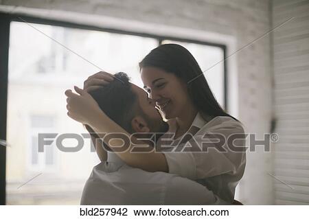 Stock Image - Caucasian couple embracing near window. Fotosearch