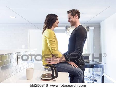 Stock Photograph - Caucasian couple embracing on kitchen counter. Fotosearch