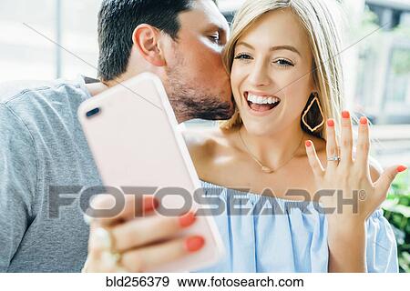 Stock Photo - Caucasian couple holding hands and posing for selfie with engagement ring. Fotosearch