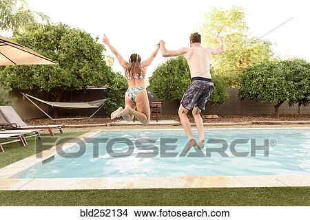 Picture - Caucasian couple holding hands jumping into swimming pool. Fotosearch
