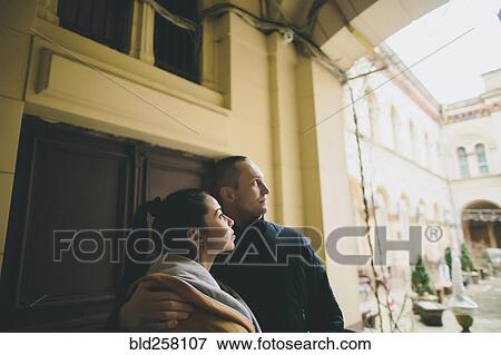 Stock Photo - Caucasian couple hugging and leaning on wall in courtyard. Fotosearch