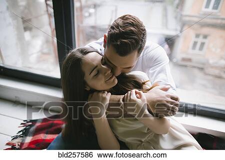 Stock Photograph - Caucasian couple hugging on bench near window. Fotosearch