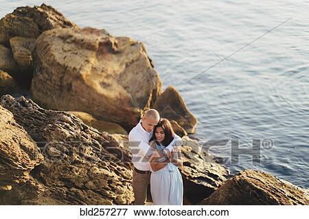 Caucasian couple hugging on rocks on beach View Large Photo Image Stock Photo - Caucasian couple hugging on rocks on beach. Fotosearch
