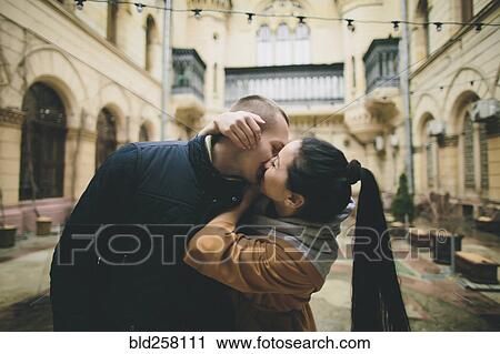 Stock Image - Caucasian couple kissing in courtyard. Fotosearch