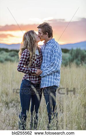 Stock Image - Caucasian couple kissing in field at sunset. Fotosearch
