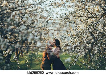 Stock Image - Caucasian couple kissing near blooming trees. Fotosearch