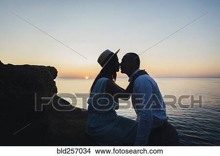 Caucasian couple kissing on rock near ocean at sunset View Large Photo Image Picture - Caucasian couple kissing on rock near ocean at sunset. Fotosearch