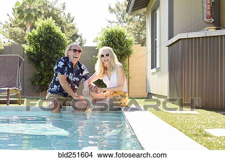 Picture - Caucasian couple laughing with legs in swimming pool. Fotosearch