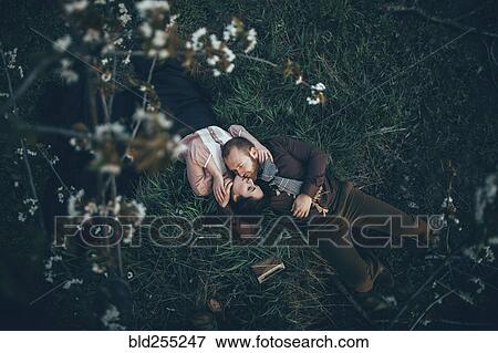 Stock Photo - Caucasian couple laying in grass and kissing. Fotosearch