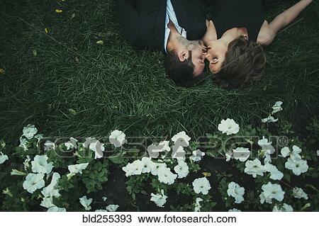 Stock Image - Caucasian couple laying in grass kissing. Fotosearch