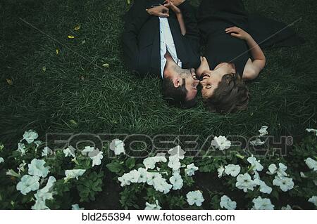 Picture - Caucasian couple laying in grass laughing. Fotosearch