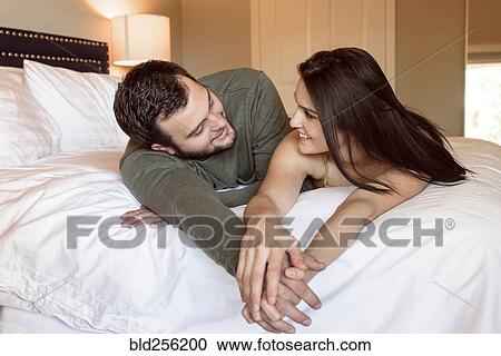 Stock Image - Caucasian couple laying on bed holding hands. Fotosearch