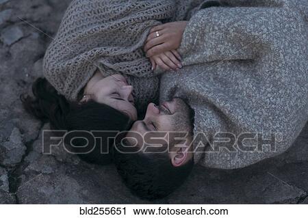 Stock Image - Caucasian couple laying on rock wrapped in blanket. Fotosearch