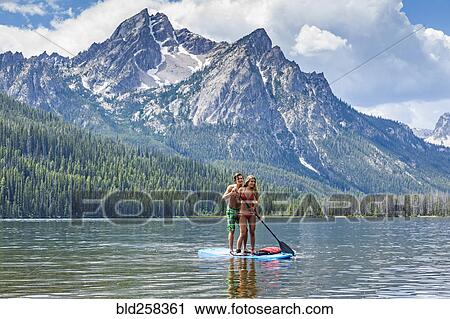 Stock Image - Caucasian couple on paddleboard in lake. Fotosearch