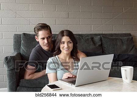 Picture - Caucasian couple on sofa using laptop. Fotosearch