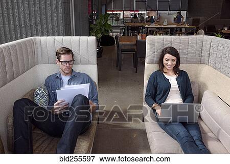 Stock Photo - Caucasian couple on sofas using laptop and reading paperwork. Fotosearch