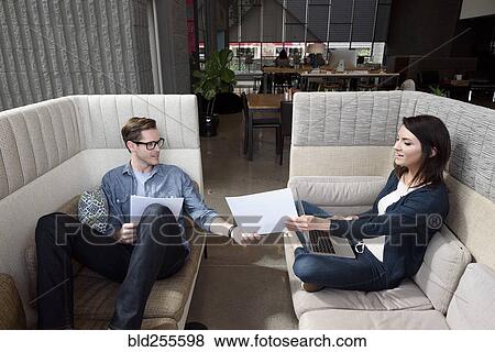 Stock Photo - Caucasian couple on sofas using laptop and reading paperwork. Fotosearch