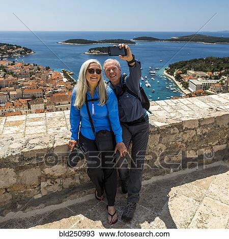 Stock Image - Caucasian couple posing for cell phone selfie with scenic view of ocean. Fotosearch